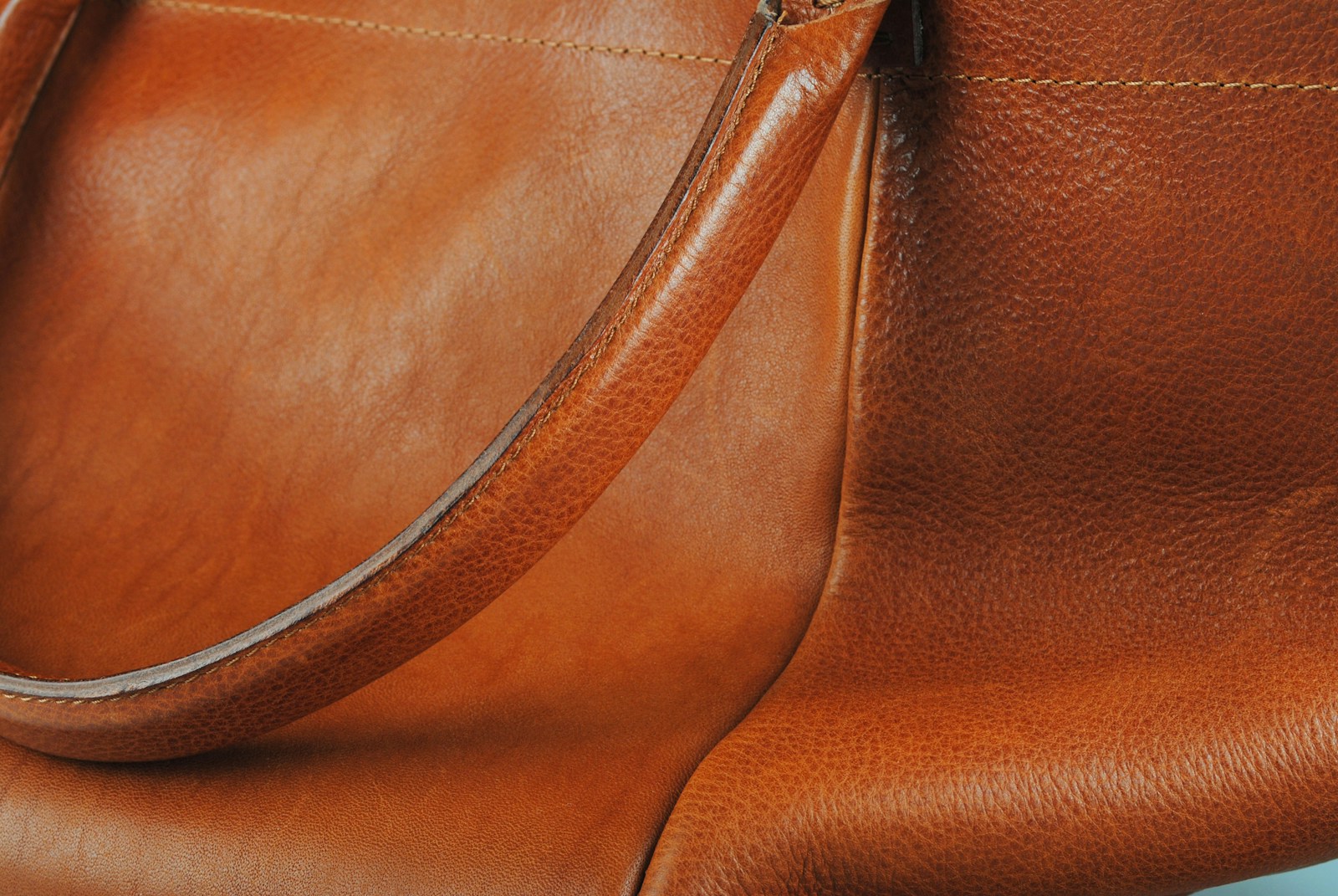 A close-up of full-grain cognac calfskin, showing the natural grain and a rolled handle.